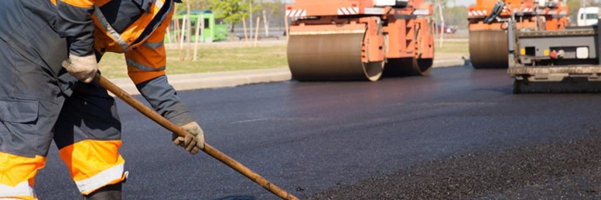 Man with reflective clothing evening out fresh asphalt with two roller machines in the background
