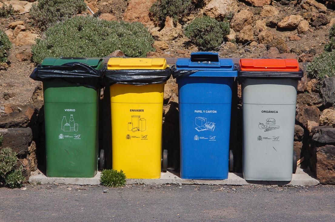 A row of compost, recycling, and waste bins outdoors along a path